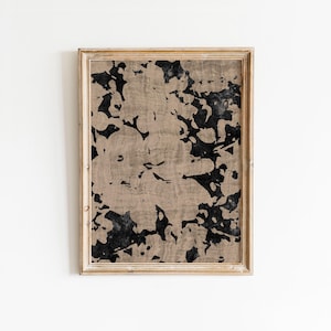Puede incluir: Impresión artística abstracta en un marco de madera. La obra presenta un patrón beige y negro con formas orgánicas. El marco es de color marrón claro. La impresión es una pieza decorativa de arte mural.