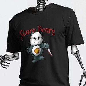 Könnte beinhalten: Schwarzes T-Shirt mit dem Text "Scare Bears" in roter Schrift. Das Shirt zeigt einen Cartoon-Bären, der ein Messer hält. Das Bild zeigt ein Skelett, das das Shirt trägt.