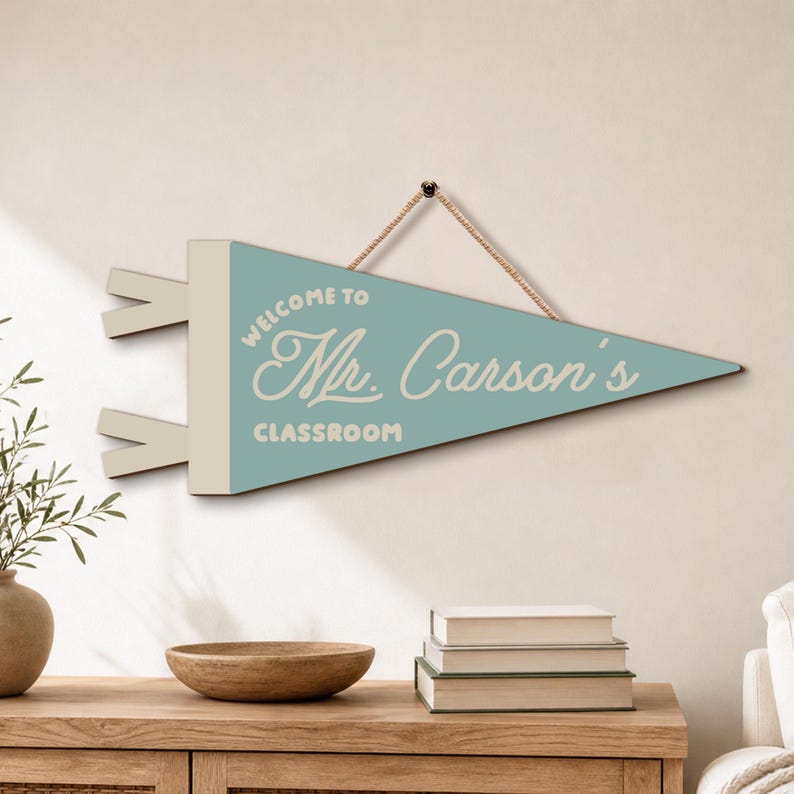 May include: A triangular wall pennant in light blue with a cream-colored side strip and two small tabs. The text reads "WELCOME TO Mr. Carson's CLASSROOM" in white lettering. A thin brown rope is attached to the top for hanging purposes.
