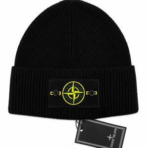 May include: Black knitted beanie hat with a rectangular patch displaying a yellow and green compass rose logo. The beanie has a ribbed texture and a hang tag with the brand name and logo.
