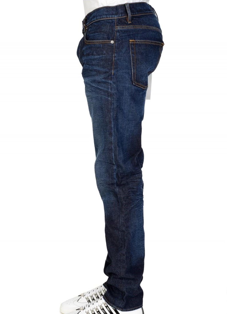 May include: Dark wash denim jeans with a classic five-pocket design. The jeans have a straight leg fit and are worn with white sneakers. The denim has a slight fade and subtle texture.