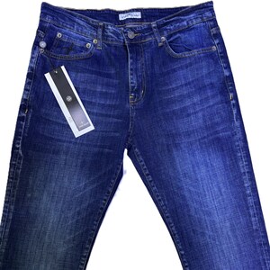 May include: Dark blue denim jeans with a classic five-pocket design. The jeans have a button and zipper closure, belt loops, and a small tag attached to the front pocket. The denim has a faded wash effect.