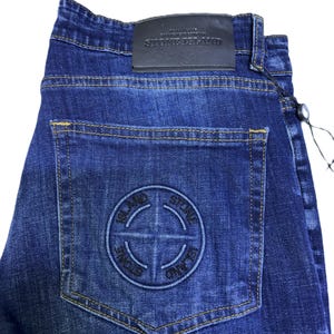 May include: Dark blue denim jeans with a classic five-pocket design. Features a leather patch with "STONE ISLAND" branding and a circular logo on the back pocket. The jeans have a straight leg cut and a button and zipper closure.