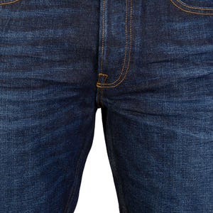 May include: Close-up of dark blue denim jeans. The jeans feature classic five-pocket styling with orange stitching. The fly has a button closure, and the rivets and button are silver. The fabric has a textured appearance.