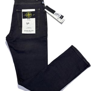 May include: Dark navy blue denim jeans with a straight leg cut. The jeans feature a back pocket with a yellow and black logo patch and a white tag. The size is 30. The jeans are new with tags.