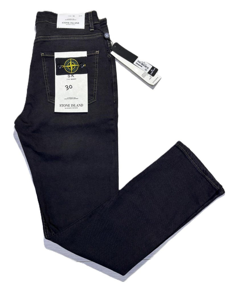 May include: Dark navy blue denim jeans with a straight leg cut. The jeans feature a back pocket with a yellow and black logo patch and a white tag. The size is 30. The jeans are new with tags.