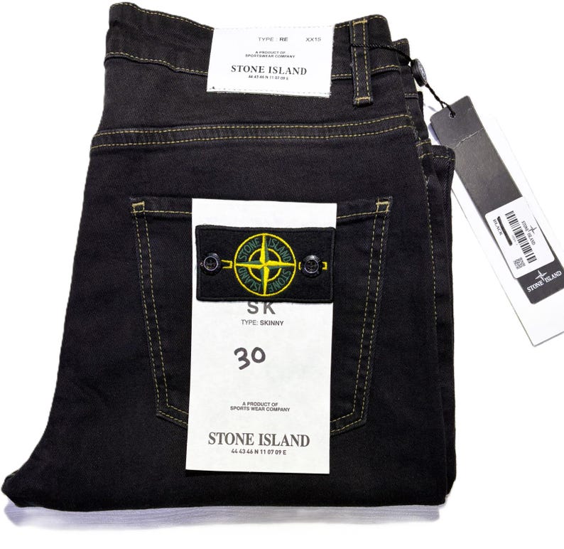 May include: Black skinny jeans with yellow stitching, featuring a Stone Island patch on the back pocket. The jeans have a size 30 label and a Stone Island tag. The jeans are folded neatly.