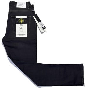 May include: Dark gray denim jeans with a tag that reads "Stone Island." The jeans have a classic five-pocket design and a straight leg. The tag indicates a size 30 waist. The jeans are new with tags.