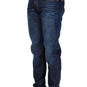 May include: Dark wash denim jeans with a classic five-pocket design. The jeans have a straight leg fit and are worn with white sneakers. The denim has a slight fade and subtle texture.