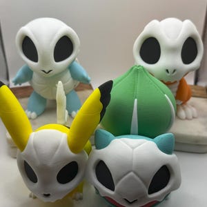 May include: A collection of 3D-printed figurines, featuring stylized designs of popular characters. The figurines showcase a variety of colors, including yellow, blue, green, and white. The figures are arranged on a white surface.