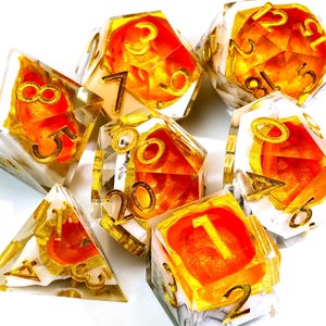 Può includere: Set di sette dadi poliedrici. Ogni dado è trasparente con una base bianca marmorizzata, accenti arancioni e dorati e numerazione dorata. I dadi sono progettati per giochi di ruolo da tavolo.
