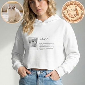 Puede incluir: Sudadera corta blanca con el nombre "LUNA" impreso en la parte delantera, junto con una definición. También hay una pequeña foto de un gato impresa en la sudadera. También es visible un gráfico circular con el texto "By REAL Artists! Ships from USA".
