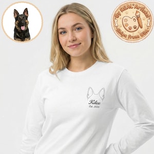 Puede incluir: Camiseta blanca de manga larga con un contorno negro de la cabeza de un perro, el nombre "Kilee" y el año "Est. 2026". Una imagen circular de un perro pastor alemán está en la esquina superior izquierda. Un logotipo circular que dice "By Real Artists!" está en la esquina superior derecha.