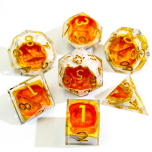 May include: A collection of seven polyhedral dice with a transparent resin exterior, showcasing orange and gold detailing. The dice are numbered in gold and are suitable for tabletop role-playing games. The set includes different shapes, such as a d4, d6, d8, d10, d12, and d20.