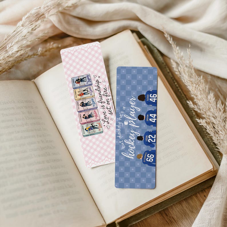 May include: Two decorative bookmarks rest on an open book. One bookmark features a pink gingham pattern and the text "Love is friendship set on fire." The other bookmark has a blue background with hockey player graphics and numbers.