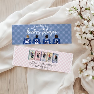 May include: Two decorative bookmarks. The top one is blue with a hockey theme, featuring the text "but daddy he's a hockey player" and player names and numbers. The bottom bookmark is pink and white with book covers and the text "Love is friendship set on fire."