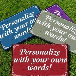 Puede incluir: Cuatro letreros rectangulares con el texto "¡Personaliza con tus propias palabras!" en blanco. Los letreros son azules, grises, morados y rojos, con bordes blancos decorativos. Los letreros están colocados sobre hierba verde.