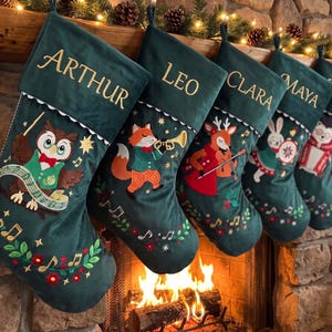 May include: Five dark green velvet Christmas stockings featuring embroidered names Arthur, Leo, Clara, Maya, and David. Each stocking displays a different woodland animal playing a musical instrument, including an owl, fox, deer, rabbit, and hedgehog.