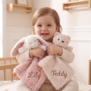 Op de afbeelding: Twee pluche knuffeldoekjes met een wit konijn en een lichtbruine beer. Het konijnendoekje is oudroze met de naam Lily in bruin geborduurd, en het beertjesdoekje is lichtbeige met de naam Teddy in bruin geborduurd.