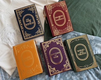 May include: Five hardcover books with gold lettering and decorative borders. The books are in various colors: navy blue, burgundy, orange, purple, and green. The titles include "The Way of Kings," "Words of Radiance," "Oathbringer," "Rhythm of War," and "Wind and Truth."