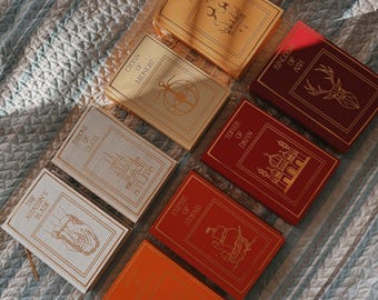 May include: A collection of fantasy novels with colorful covers. Titles include "Heir of Fire," "Crown of Midnight," "Throne of Glass," "The Assassin's Blade," "Empire of Storms," and "Kingdom of Ash." The books are arranged on a patterned surface.