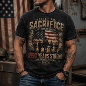 Puede incluir: Una camiseta negra de manga corta con un estampado gr&aacute;fico que incluye el texto BUILT ON SACRIFICE, FORGED IN HONOR, 250 YEARS STRONG y HONOR COURAGE COMMITMENT. El dise&ntilde;o muestra una bandera estadounidense desgastada y cinco soldados.
