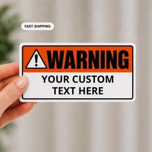 Peut inclure: Un autocollant d'avertissement rectangulaire avec une section supérieure orange comportant un triangle noir avec un point d'exclamation et le mot WARNING en noir. La section inférieure blanche contient le texte noir YOUR CUSTOM TEXT HERE.