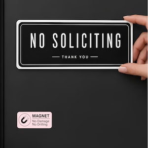 Könnte beinhalten: Ein rechteckiges schwarzes Schild mit weißem Rand und dem weißen Text NO SOLICITING sowie THANK YOU. Darunter befindet sich ein kleines hellrosa rechteckiges Etikett mit einem Magnetsymbol und dem Text MAGNET, No Damage, No Drilling.