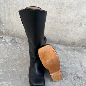 K&ouml;nnte beinhalten: Ein Paar schwarze Lederstiefel mit quadratischer Spitze und hohem Schaft. Ein Stiefel steht aufrecht, w&auml;hrend der andere auf der Seite liegt und die hellbraune Sohle freilegt. Die Stiefel scheinen neu zu sein.