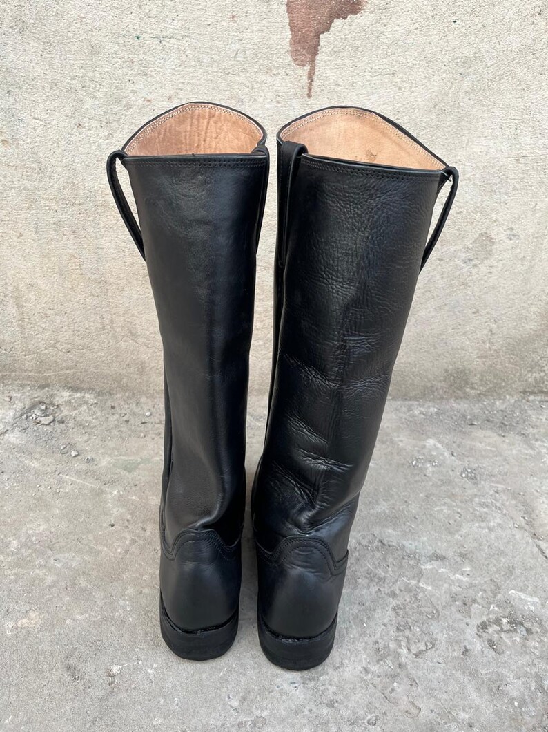 K&ouml;nnte beinhalten: Ein Paar schwarze Lederreitstiefel. Die Stiefel sind hoch, reichen bis zur Mitte der Wade und haben eine glatte, polierte Oberfl&auml;che. Sie haben ein klassisches Design mit runder Spitze und kleinem Absatz. Das Innenfutter ist hellbraun.
