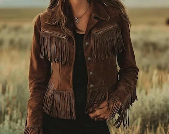 May include: Brown suede jacket with fringe detailing on the chest, sleeves, and hem. The jacket has a button-up front and a collared neckline. The model is wearing a black top and pants. The background is a field of tall grass.