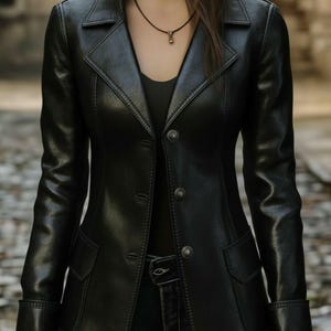 Peut inclure: Un blazer en cuir noir au design classique. La veste présente un col cranté, une fermeture à trois boutons, deux poches avant et des manches longues avec des poignets boutonnés. Le blazer est porté sur un haut noir et un jean bleu.