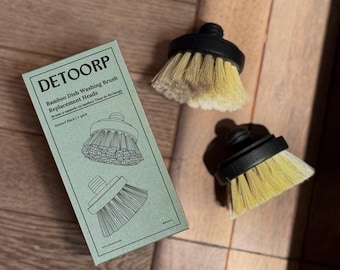 May include: A package of DETOORP bamboo dish washing brush replacement heads, stained black, with two replacement brush heads. The brush heads have a black base and light yellow bristles. The package is light green.