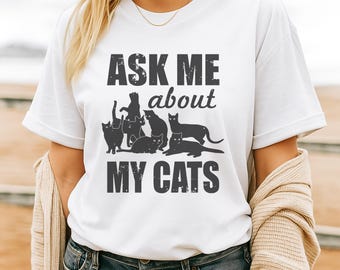 Może przedstawiać: Biała koszulka z napisem "ASK ME about MY CATS" w stylu vintage. Projekt zawiera czarne sylwetki kotów. Codzienny, swobodny element garderoby.