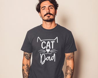 May include: Dark gray t-shirt with the words "CAT Dad" in white, featuring a cat face design. The shirt is a crew neck and has short sleeves. The text is centered on the chest.