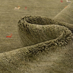 May include: Close-up of a rolled-up olive green rug with a textured surface. The rug has small, scattered designs in red and white. The rug's fibers are visible, creating a soft, inviting appearance.