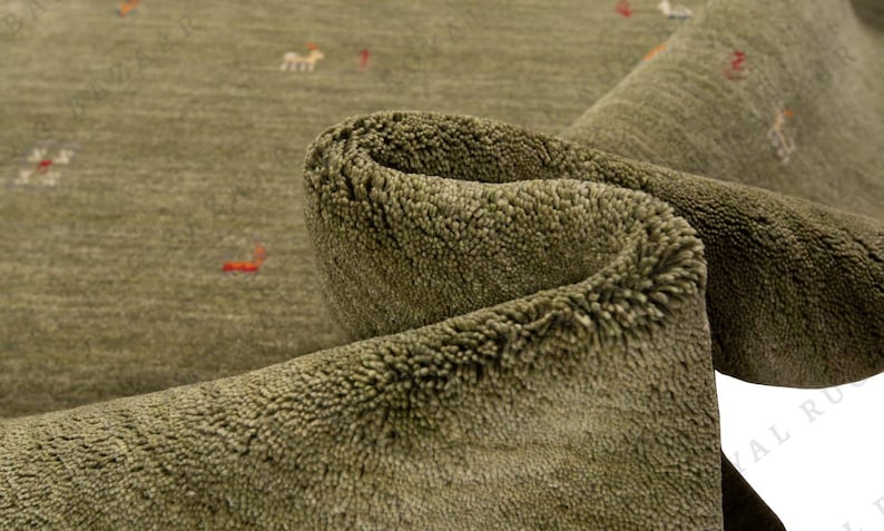 May include: Close-up of a rolled-up olive green rug with a textured surface. The rug has small, scattered designs in red and white. The rug's fibers are visible, creating a soft, inviting appearance.