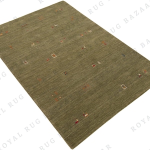 May include: A rectangular olive green rug with a textured surface. The rug features small, scattered geometric shapes in various colors, including red, white, and brown. The rug is a floor covering.