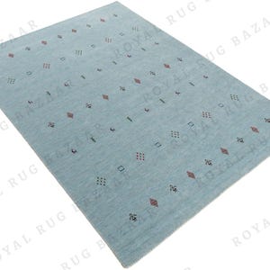 May include: A rectangular, light blue rug with a repeating pattern of small geometric shapes in red, black, and green. The rug has a soft, textured appearance and is suitable for a living room or bedroom.