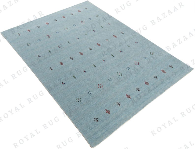 May include: A rectangular, light blue rug with a repeating pattern of small geometric shapes in red, black, and green. The rug has a soft, textured appearance and is suitable for a living room or bedroom.