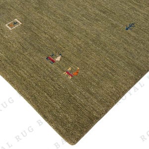 May include: Olive green area rug with a textured surface and small, colorful geometric designs. The rug's corner is visible, showcasing its woven construction and earthy tones. The rug's dimensions are not visible.