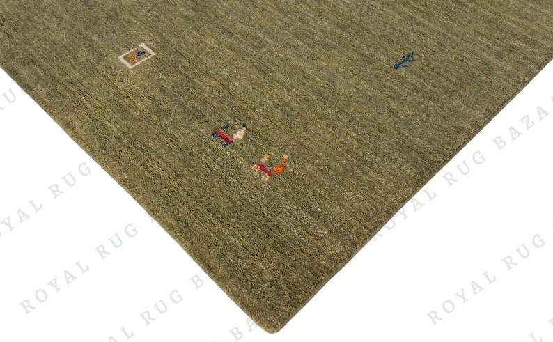 May include: Olive green area rug with a textured surface and small, colorful geometric designs. The rug's corner is visible, showcasing its woven construction and earthy tones. The rug's dimensions are not visible.