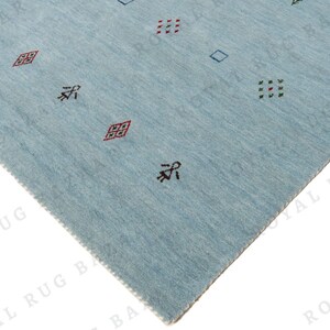May include: A light blue rug with a geometric pattern. The rug features small, repeating designs in red, green, and black. The rug's texture is visible, and the edges are neatly finished. The overall design is simple and modern.