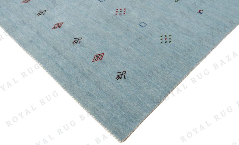 May include: A light blue rug with a geometric pattern. The rug features small, repeating designs in red, green, and black. The rug's texture is visible, and the edges are neatly finished. The overall design is simple and modern.