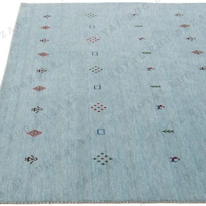 May include: A light blue rug with a repeating pattern of geometric shapes in red, green, and blue. The rug has a soft texture and a simple, modern design, suitable for a living room or bedroom.