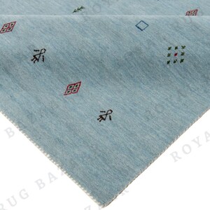 May include: A light blue rug with a geometric pattern. The rug has a triangular shape with a folded corner, revealing a lighter underside. Small, colorful geometric shapes are scattered across the surface.