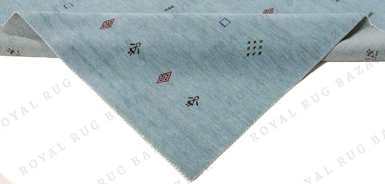 May include: A light blue rug with a geometric pattern. The rug has a triangular shape with a folded corner, revealing a lighter underside. Small, colorful geometric shapes are scattered across the surface.