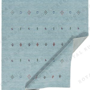 May include: A light blue rug with a repeating pattern of small geometric shapes and figures in red, green, and blue. The rug is folded over, revealing a lighter underside. The overall design is simple and modern.