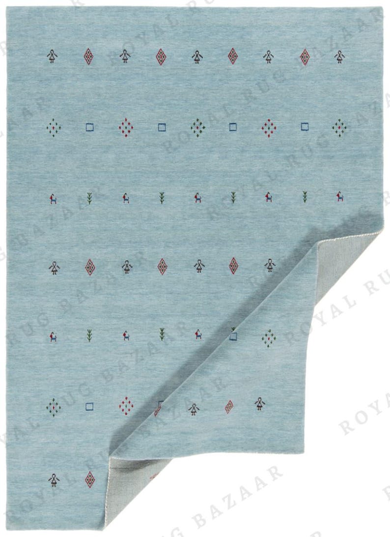 May include: A light blue rug with a repeating pattern of small geometric shapes and figures in red, green, and blue. The rug is folded over, revealing a lighter underside. The overall design is simple and modern.