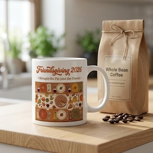 May include: A white ceramic mug featuring the text Friendsgiving 2026 and I Brought the Pie (and the Drama) above a colourful illustration of a Thanksgiving table setting with plates, silverware, wine glasses, pumpkins, and autumn leaves.